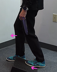 Image of Tara Tobias from the waist down, standing with her left foot on a foam wedge, heel down and right foot forward, demonstrating a calf stretch on the affected leg.